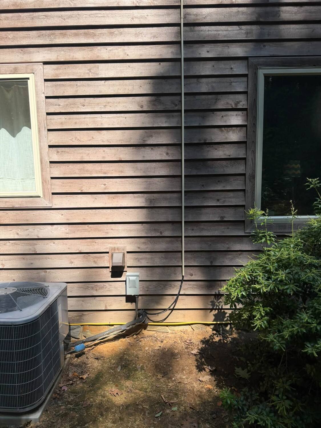 Exterior low-voltage raceway routed down wood siding to equipment near the electrical disconnect