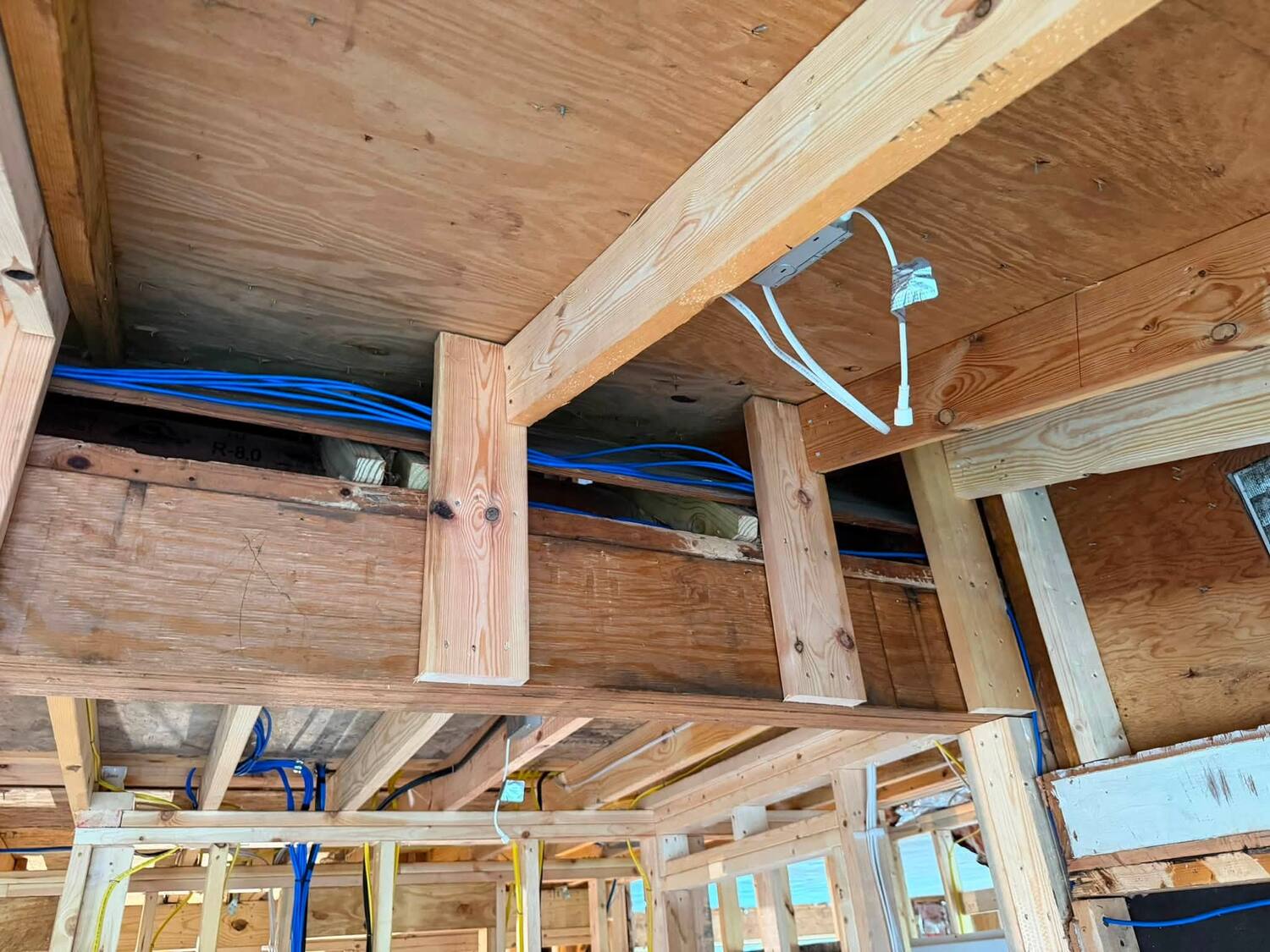 Blue and yellow low-voltage cable runs along an attic knee-wall with Rmax insulation board during a prewire