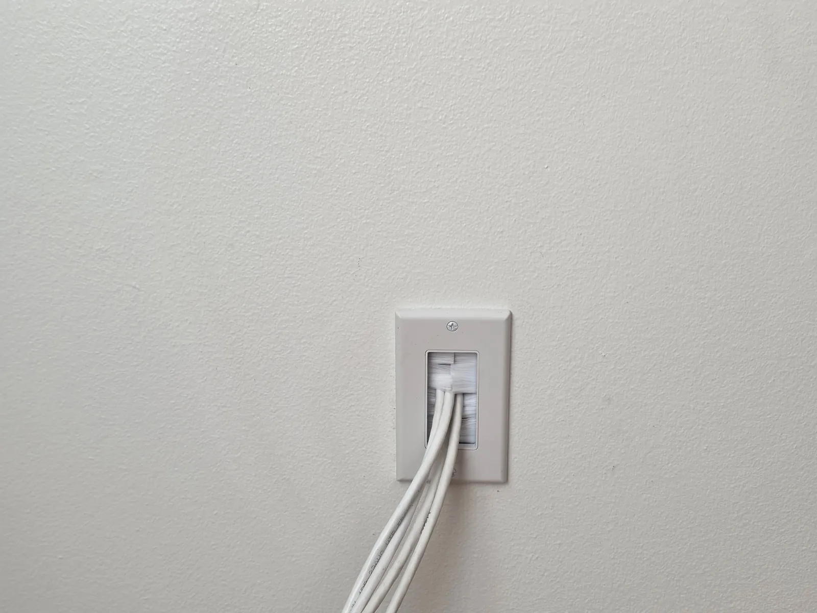 Close-up of a brush wall plate with security camera cables entering the wall